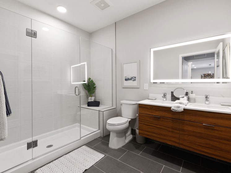 Large bathroom with couple's vanity featuring two sinks and light-up mirror and walk-in shower with bench